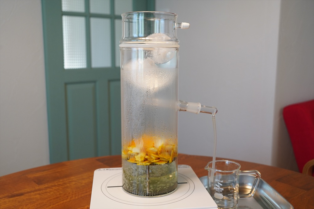 蒸留中のガラス製蒸留器から芳香蒸留水がビーカーに落ちる様子